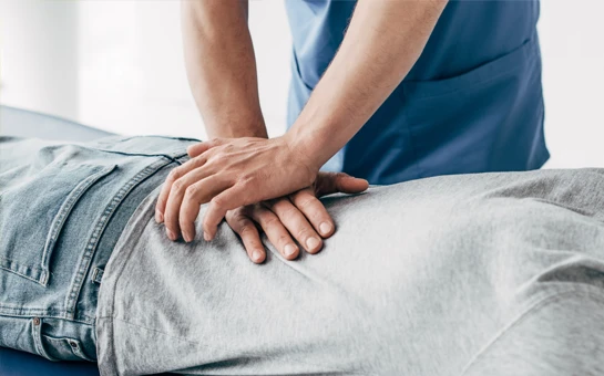 A chiropractor delivering a back adjustment to a patient laying face down on an adjustment table